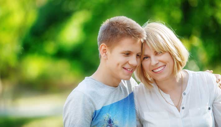 نوجوان لڑکا اپنی ماں کے ساتھ مسکراتا ہوا ، ایک بازو سے گلے لگا رہا ہے۔