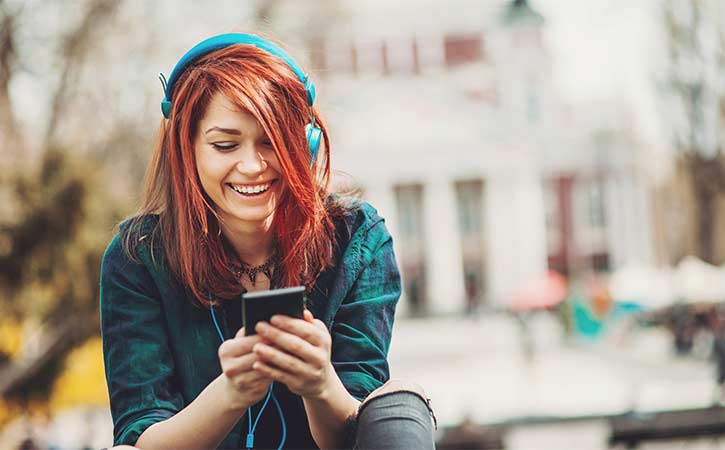 Giovane donna che sorride ascoltando musica e guardando il suo telefono
