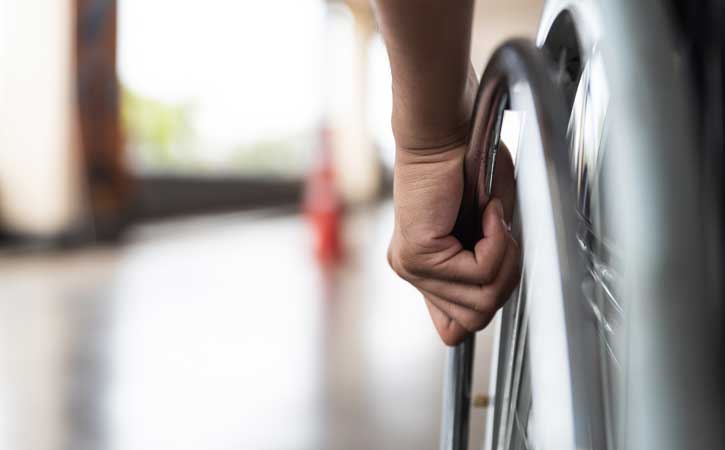 Изображение крупным планом человека, держащего шину инвалидной коляски, вид левой руки, держащей колесо