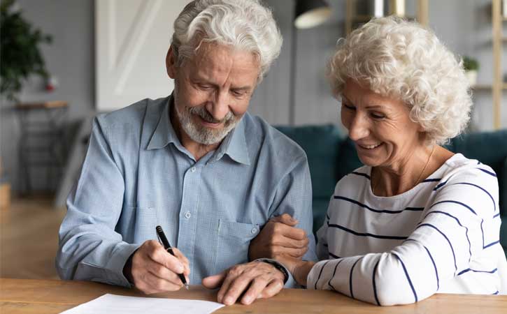 Elderly couple, arms linked, smiling while signing a document