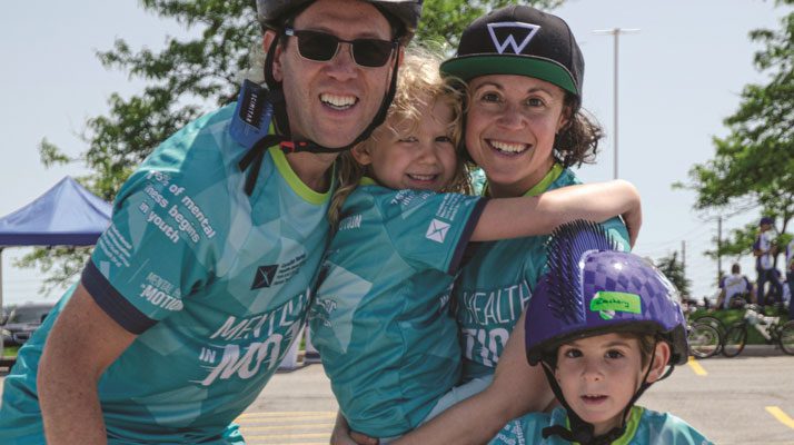 family smiling at a fundraiser with mother holding her daughter and son wearing a helmet