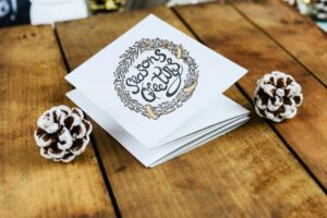 Seasons greeting card on a table with pinecones on each side