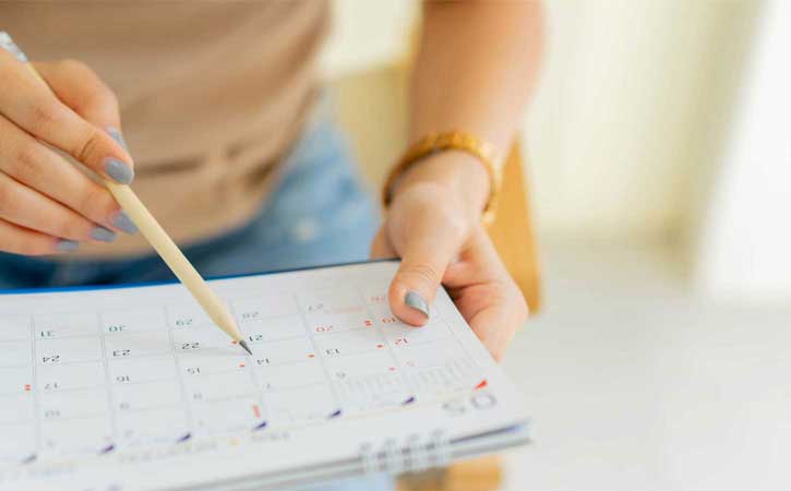 Imagen de primer plano de manos con uñas pintadas sosteniendo un lápiz y un calendario