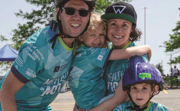 Family of four: a male, female and two children, smiling for the camera in "Mental Health in Motion" jerseys.