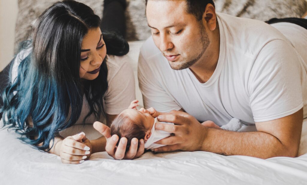 couple laying in bed holding their newborn baby in their hands