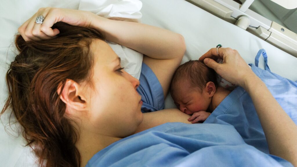 Mother in hospital bed breastfeeding newborn, dealing with postpartum mental health issues