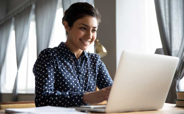 Женщина смотрит на ноутбук, с широкой улыбкой на лице
