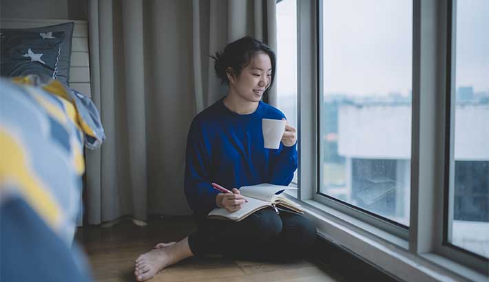 mujer sentada junto al alféizar de la ventana con café y diario en la mano