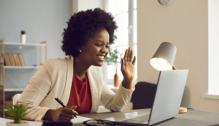 Woman waving at laptop, sitting at desk